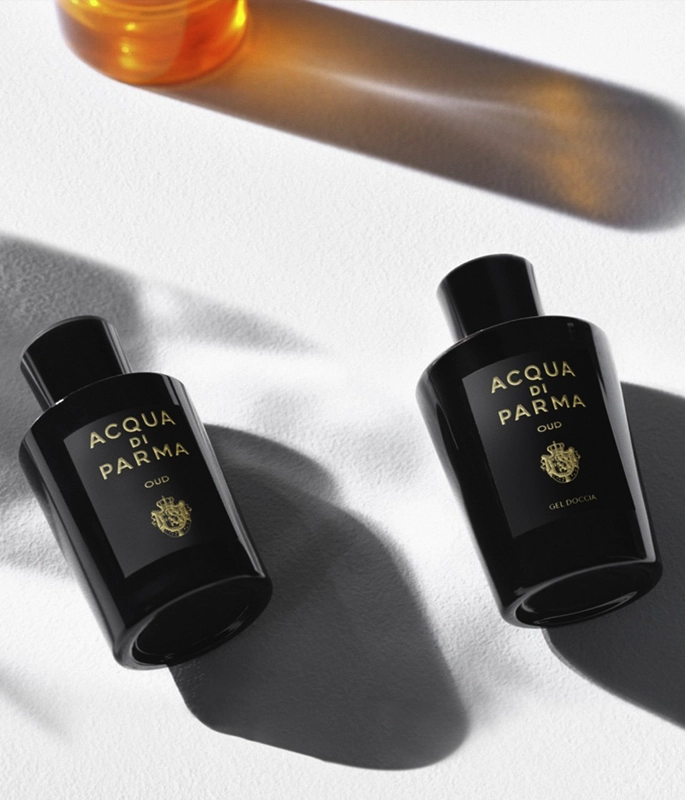 two oud acqua di parma black perfume bottles lay on side, white background, high contrast light