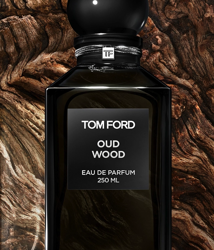 black tom ford oud wood bottle with circular stopper lid in front of wood background 